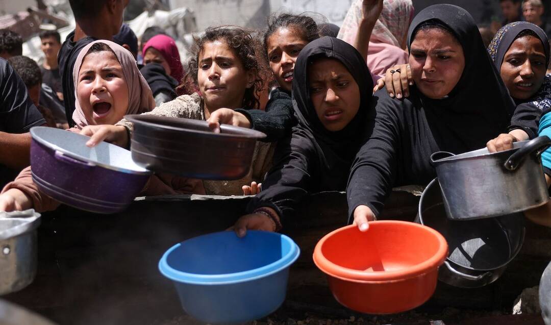 Displaced Palestinians gather to collect portions of cooked food at a charity distribution in Jabalia in the northern Gaza Strip