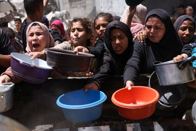 Displaced Palestinians gather to collect portions of cooked food at a charity distribution in Jabalia in the northern Gaza Strip